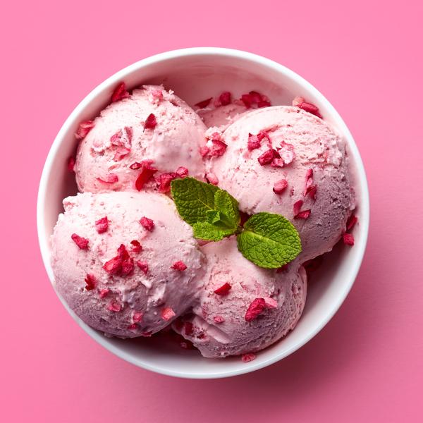Three scoops of strawberry icecream in a white bowl on pink background