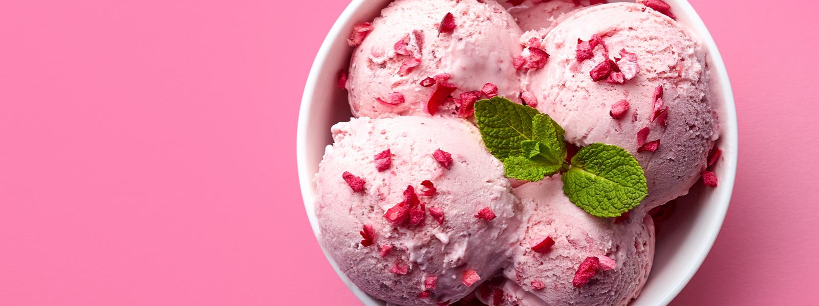 Three scoops of strawberry icecream in a white bowl on pink background