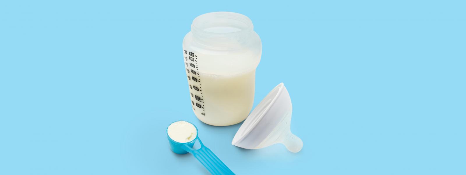 Baby bottle of milk alongside a scoop of infant nutrition formula